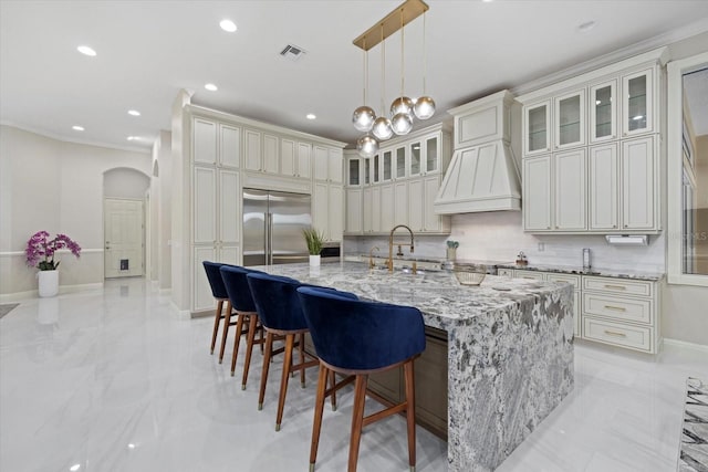 kitchen featuring built in fridge, arched walkways, custom exhaust hood, visible vents, and backsplash