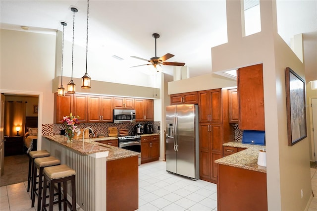 kitchen featuring kitchen peninsula, appliances with stainless steel finishes, a towering ceiling, and a kitchen breakfast bar