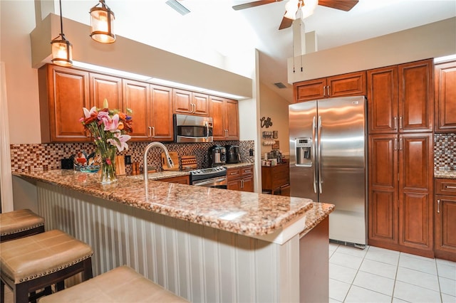 kitchen featuring hanging light fixtures, a breakfast bar area, light stone counters, kitchen peninsula, and stainless steel appliances