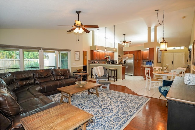 living room featuring light hardwood / wood-style flooring, high vaulted ceiling, and ceiling fan