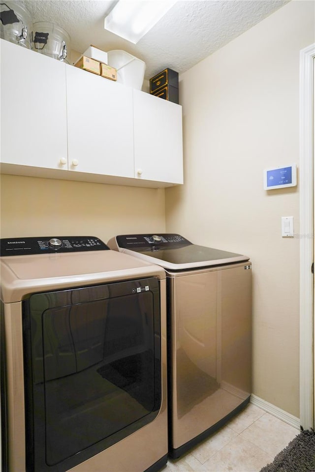 clothes washing area with cabinets, independent washer and dryer, a textured ceiling, and light tile patterned flooring