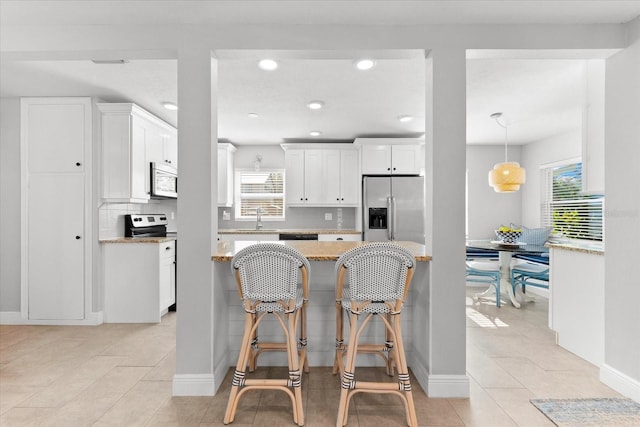 kitchen featuring stainless steel fridge, light stone counters, white cabinetry, and a wealth of natural light