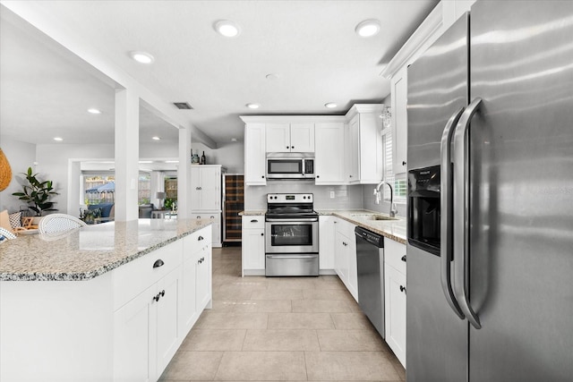 kitchen with white cabinets, sink, light stone countertops, light tile patterned flooring, and stainless steel appliances