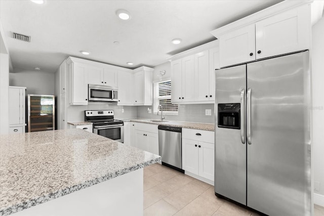 kitchen with decorative backsplash, appliances with stainless steel finishes, light stone countertops, sink, and white cabinets