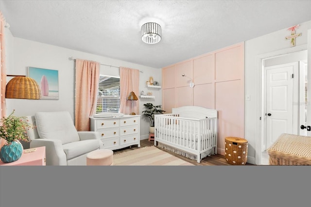 bedroom with wood-type flooring, a textured ceiling, and a nursery area