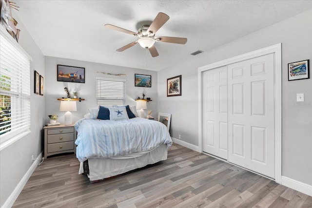 bedroom with ceiling fan, a closet, wood-type flooring, and multiple windows