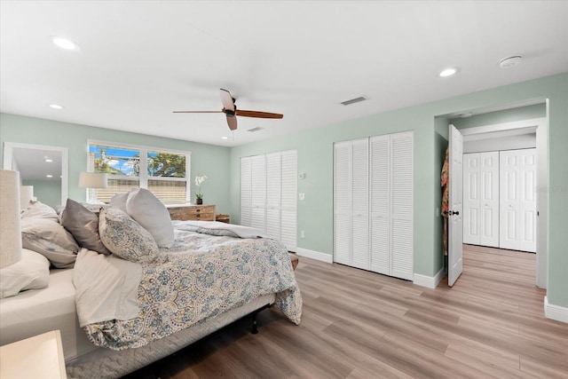 bedroom with ceiling fan, light hardwood / wood-style flooring, and two closets