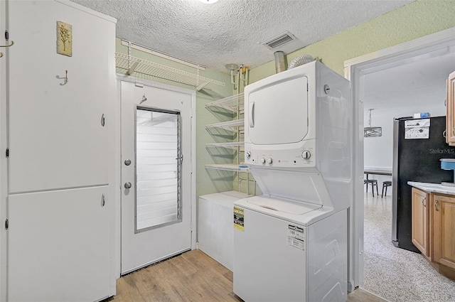 washroom featuring stacked washer / dryer, light hardwood / wood-style floors, and a textured ceiling