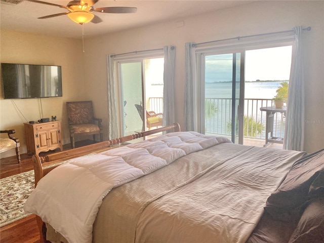 bedroom featuring access to outside, ceiling fan, a water view, and hardwood / wood-style flooring