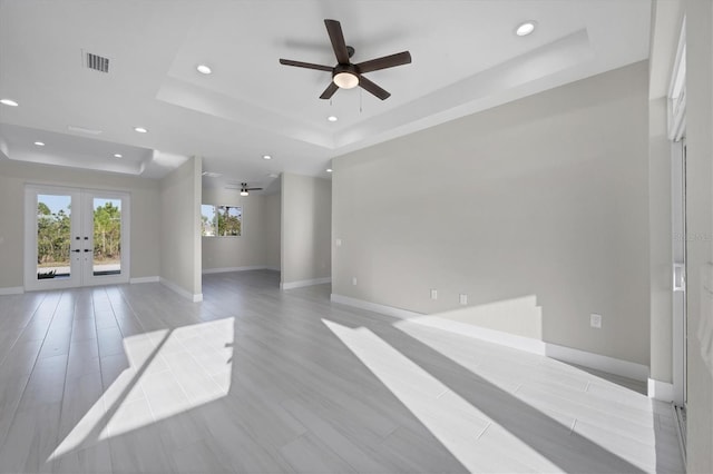 unfurnished living room featuring ceiling fan, light wood-type flooring, french doors, and a tray ceiling