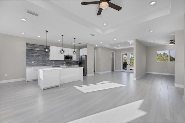 kitchen with stainless steel appliances, a kitchen island, light hardwood / wood-style flooring, white cabinetry, and hanging light fixtures