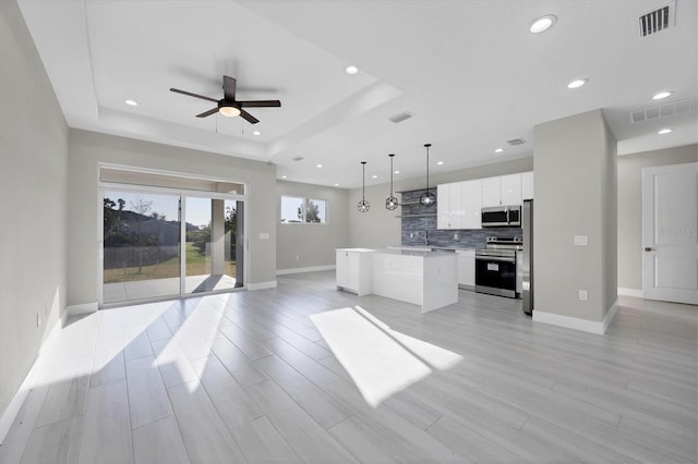 kitchen with a center island, hanging light fixtures, a tray ceiling, stainless steel appliances, and white cabinets