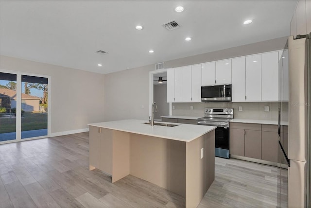 kitchen with stainless steel appliances, sink, a center island with sink, white cabinets, and light hardwood / wood-style floors