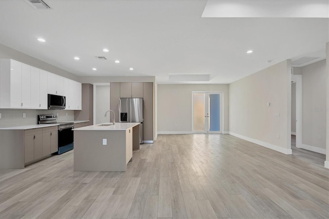 kitchen featuring sink, appliances with stainless steel finishes, an island with sink, decorative backsplash, and light wood-type flooring