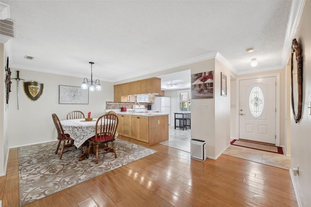 dining area featuring ornamental molding, a textured ceiling, sink, an inviting chandelier, and light hardwood / wood-style floors