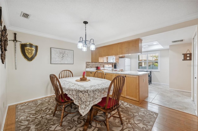 dining space with light hardwood / wood-style floors, sink, ornamental molding, and a textured ceiling