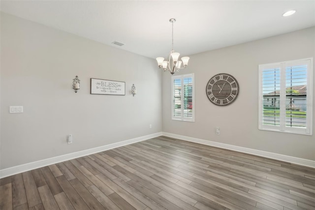 unfurnished room featuring plenty of natural light, hardwood / wood-style floors, and a notable chandelier