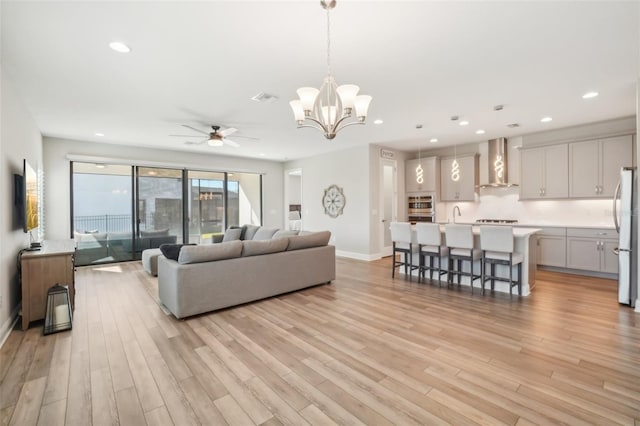 living room featuring ceiling fan with notable chandelier and light wood-type flooring