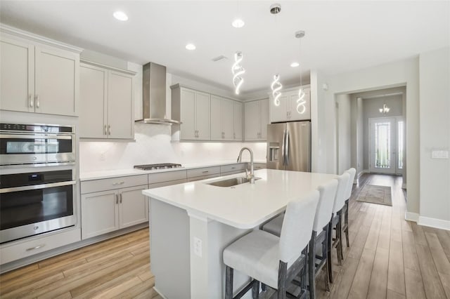 kitchen featuring wall chimney exhaust hood, sink, stainless steel appliances, and light hardwood / wood-style flooring