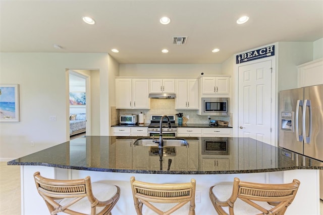 kitchen with white cabinetry, sink, dark stone countertops, a large island, and stainless steel appliances