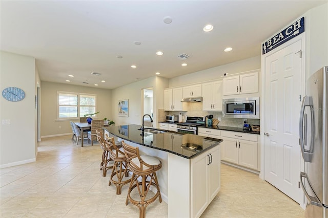 kitchen featuring sink, appliances with stainless steel finishes, an island with sink, white cabinets, and dark stone counters