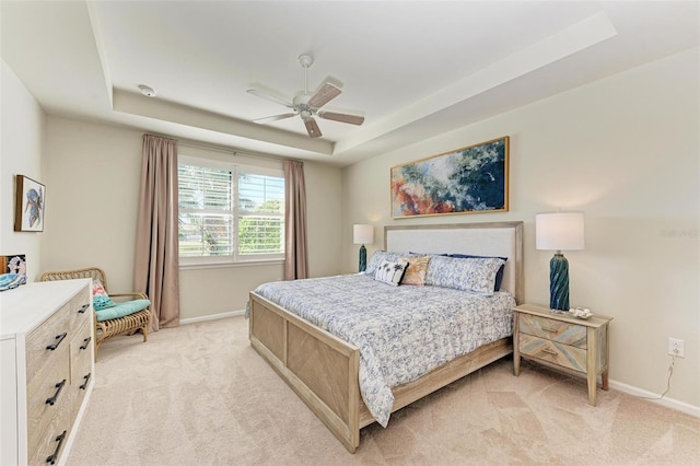 bedroom with ceiling fan, light colored carpet, and a tray ceiling