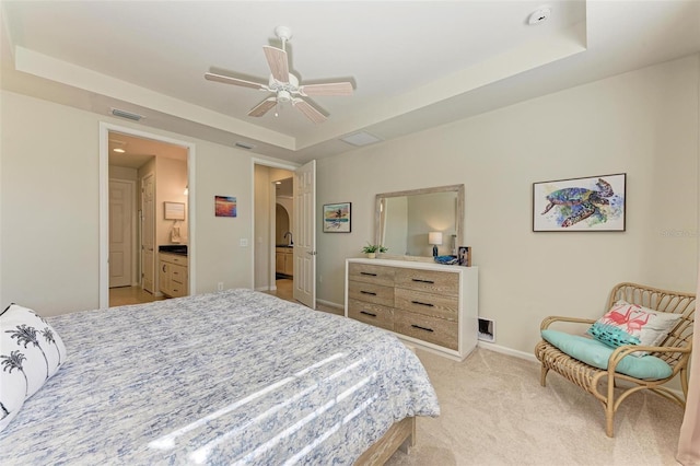 bedroom with connected bathroom, a tray ceiling, light colored carpet, and ceiling fan