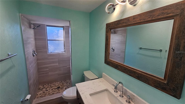 bathroom featuring a tile shower, vanity, and toilet