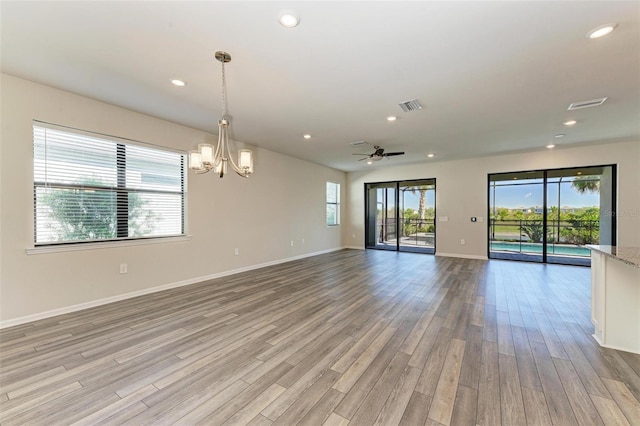 spare room with ceiling fan with notable chandelier, light wood-type flooring, and a healthy amount of sunlight