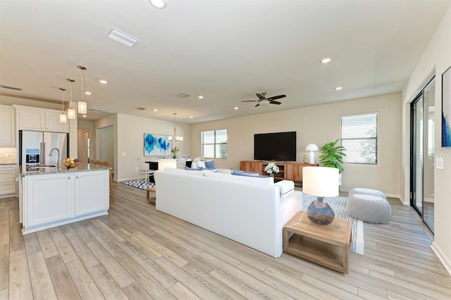 living room featuring ceiling fan with notable chandelier and light wood-type flooring