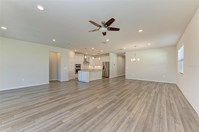 unfurnished living room with light hardwood / wood-style flooring, ceiling fan with notable chandelier, and sink