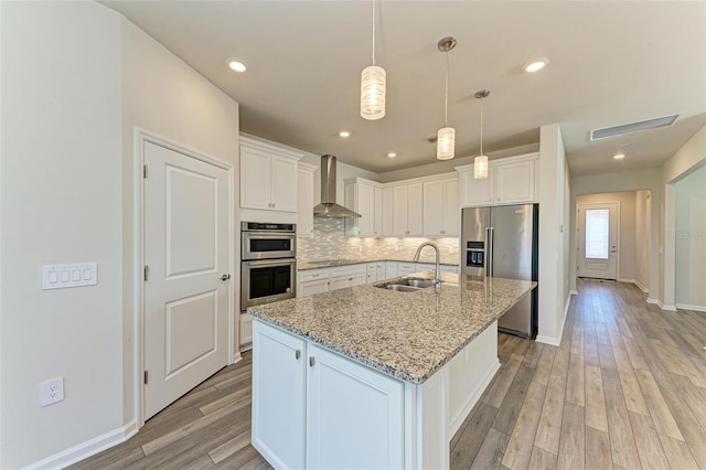 kitchen with white cabinetry, a center island with sink, wall chimney range hood, and appliances with stainless steel finishes