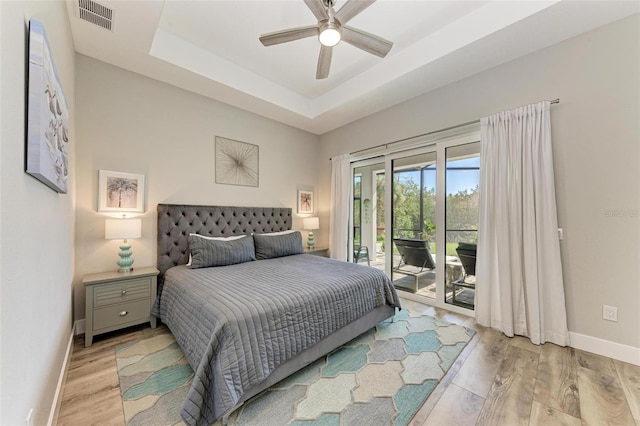 bedroom with ceiling fan, a raised ceiling, light wood-type flooring, and access to outside