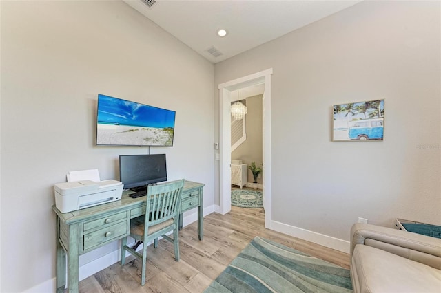 home office with light hardwood / wood-style floors, lofted ceiling, and a notable chandelier