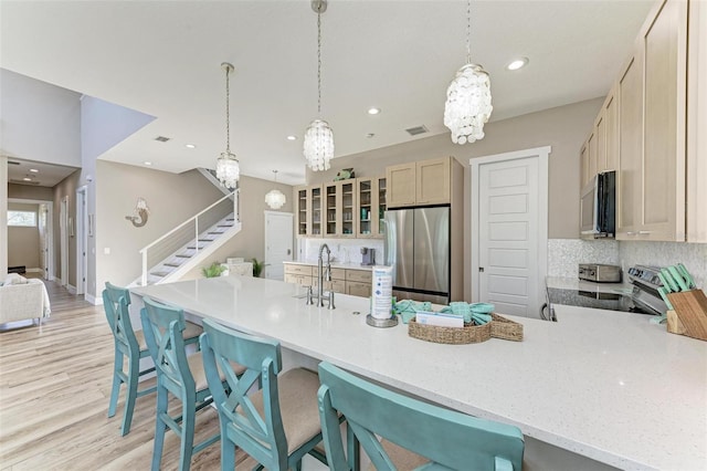 kitchen featuring kitchen peninsula, light brown cabinetry, backsplash, a kitchen breakfast bar, and stainless steel appliances