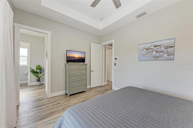 bedroom with a tray ceiling, ceiling fan, and light wood-type flooring