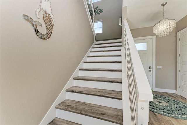 stairs featuring wood-type flooring and an inviting chandelier