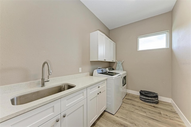 clothes washing area featuring washing machine and clothes dryer, sink, cabinets, and light hardwood / wood-style flooring