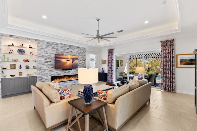 living room with a tray ceiling, ceiling fan, crown molding, light tile patterned floors, and a fireplace