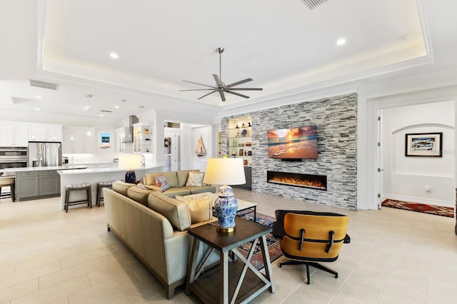 living room featuring ceiling fan, light tile patterned floors, a tile fireplace, and a tray ceiling