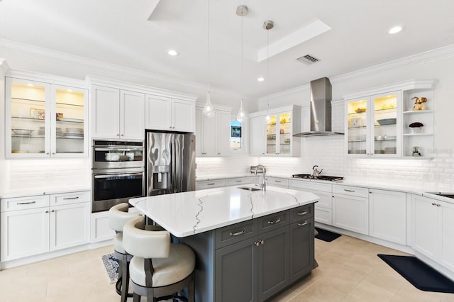 kitchen with stainless steel appliances, white cabinetry, wall chimney exhaust hood, an island with sink, and pendant lighting