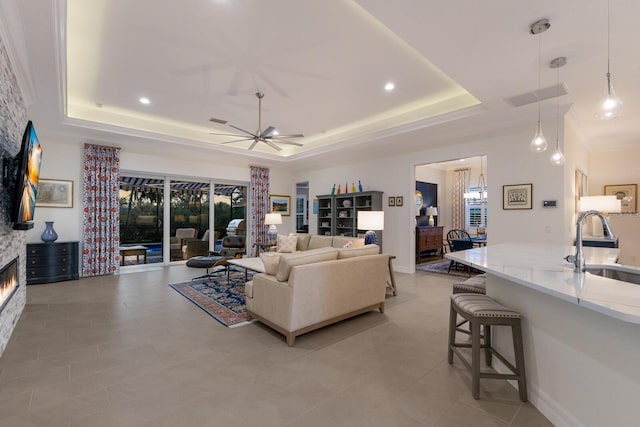 tiled living room with a fireplace, a raised ceiling, ceiling fan, and sink