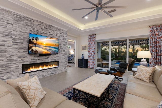 living room with a stone fireplace, ceiling fan, crown molding, and concrete flooring