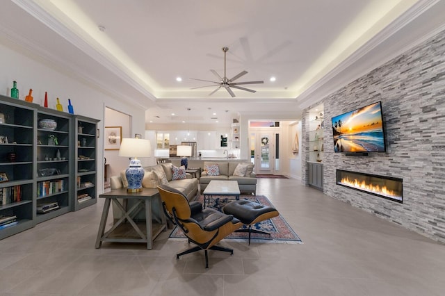 living room featuring ceiling fan, a raised ceiling, a fireplace, and crown molding