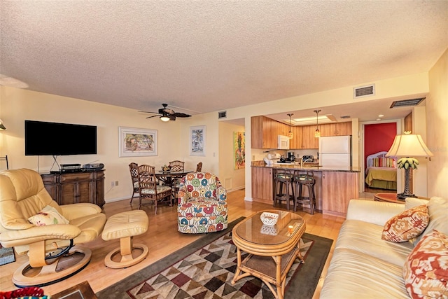 living room with ceiling fan, light hardwood / wood-style floors, and a textured ceiling