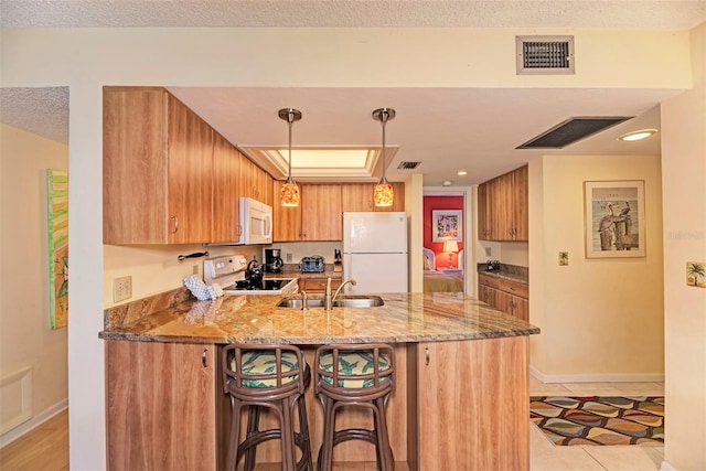 kitchen featuring kitchen peninsula, light stone countertops, white appliances, sink, and hanging light fixtures