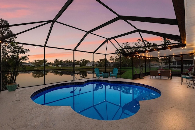 pool at dusk with glass enclosure, a patio area, and a water view