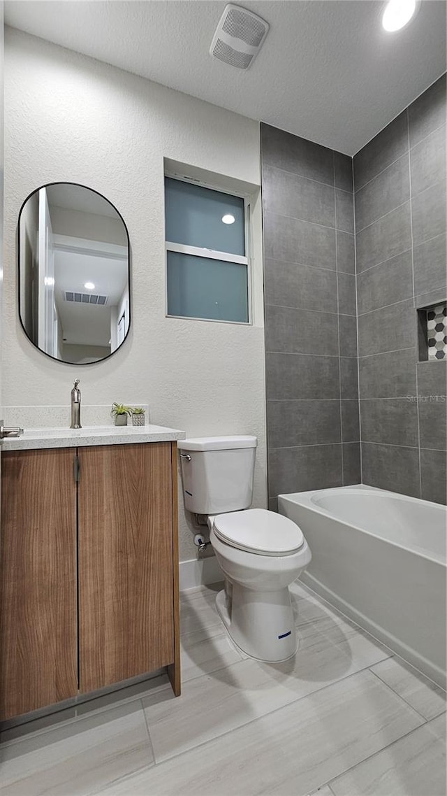 full bathroom with vanity, a textured ceiling, tiled shower / bath combo, and toilet