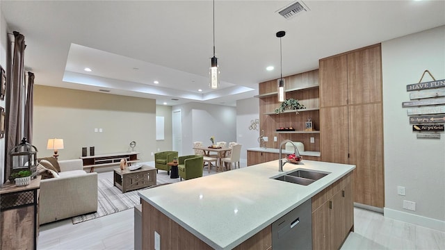 kitchen with a tray ceiling, a kitchen island with sink, sink, dishwasher, and hanging light fixtures