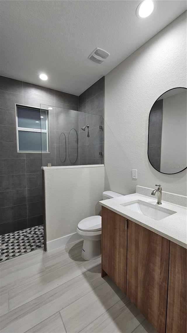 bathroom featuring toilet, vanity, a textured ceiling, and tiled shower